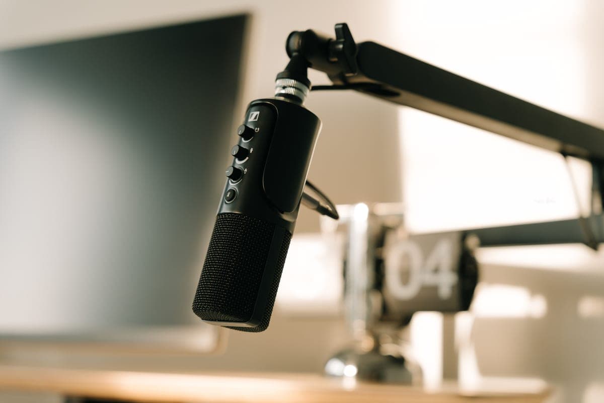 A broadcast-style dynamic microphone on a desk boom arm in a home studio