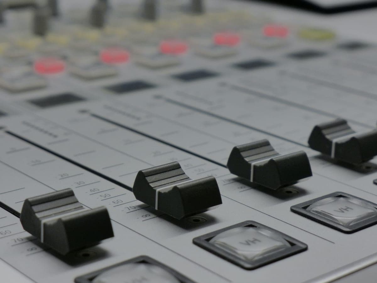 A multi-channel podcast mixing console with faders on a studio desk